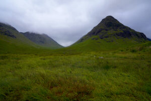 Lofty green peaks rise above the emerald sea of grass and heather in Glen Coe, nearly touching the clouds.