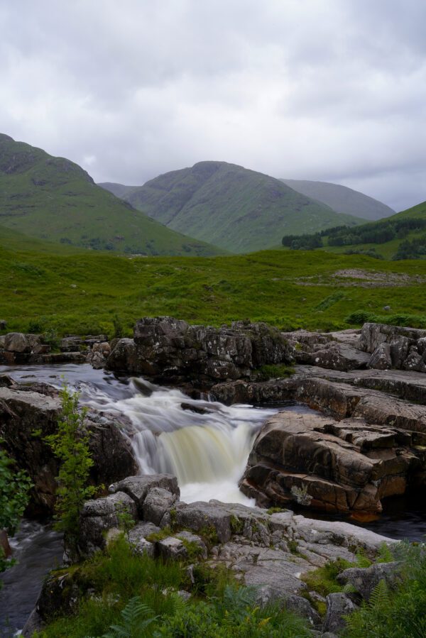 A waterfall pours over a short cliff in stunning Glen Etive, Scotland.