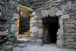 A stone wall in the ruins of Lochranza Castle has two doorways - dark on the right, lit by sun on the left.