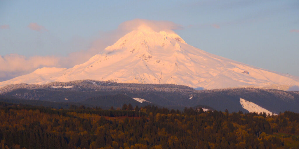 Warm sunset light bathes the slopes of snowy Mt Hood as seen from Jonsrud Viewpoint in Sandy, Oregon.