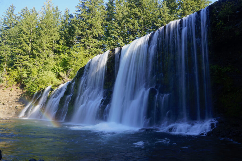 A rainbow lights up the base of wide Upper Rock Creek Falls in Washington State.
