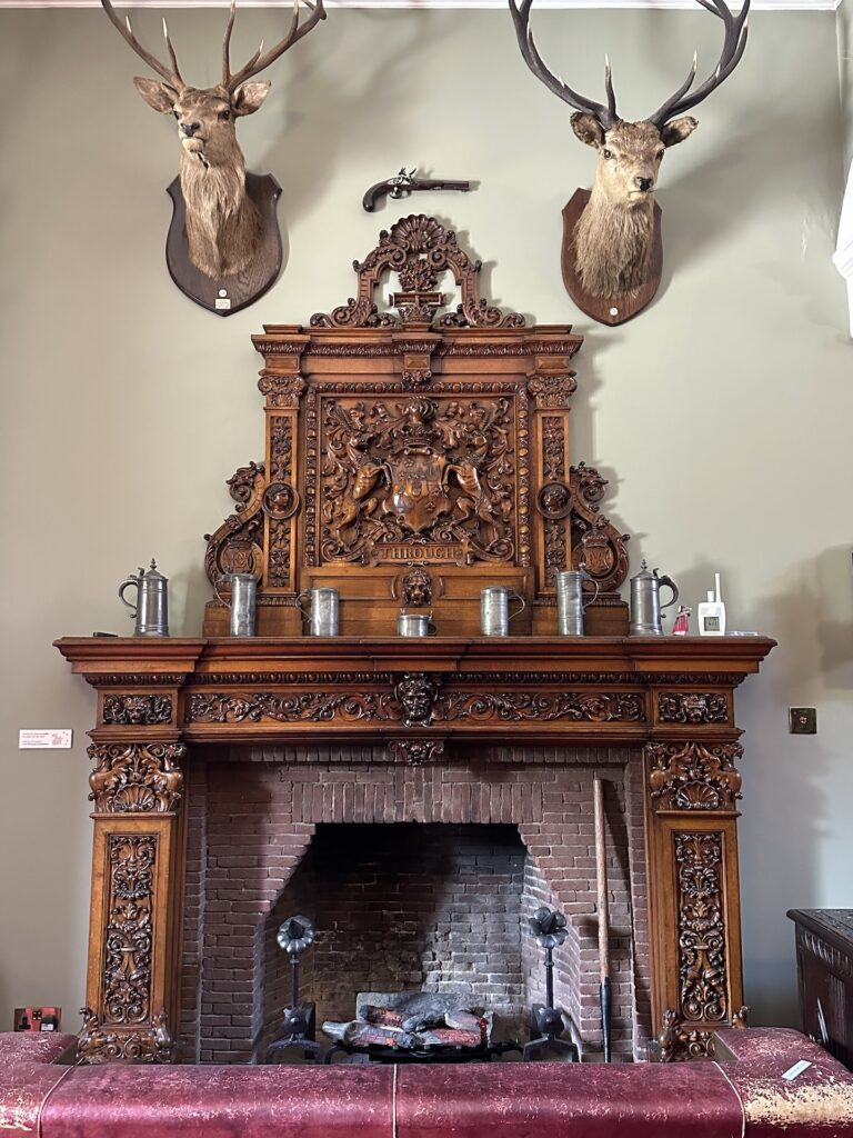 An ornately carved wooden mantle surrounds a fireplace in Brodick Castle, Scotland.