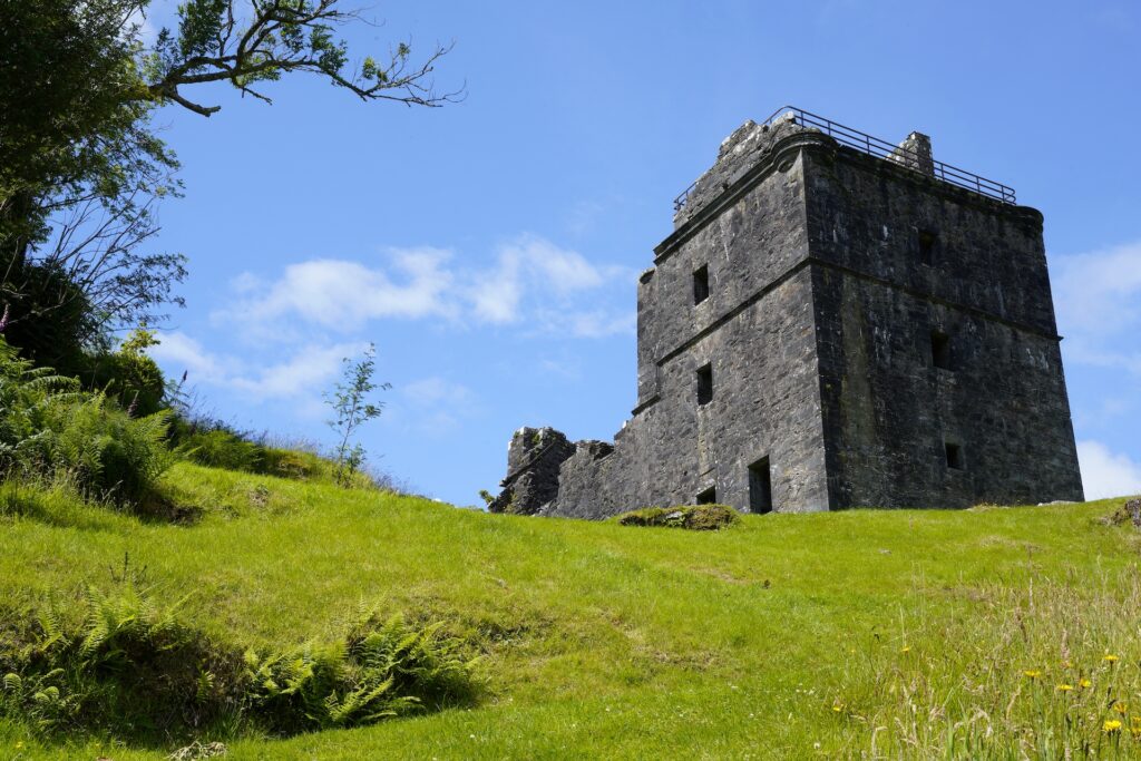 A view looking up a grassy hillside. The ruins of Carnasserie Castle are at the top.