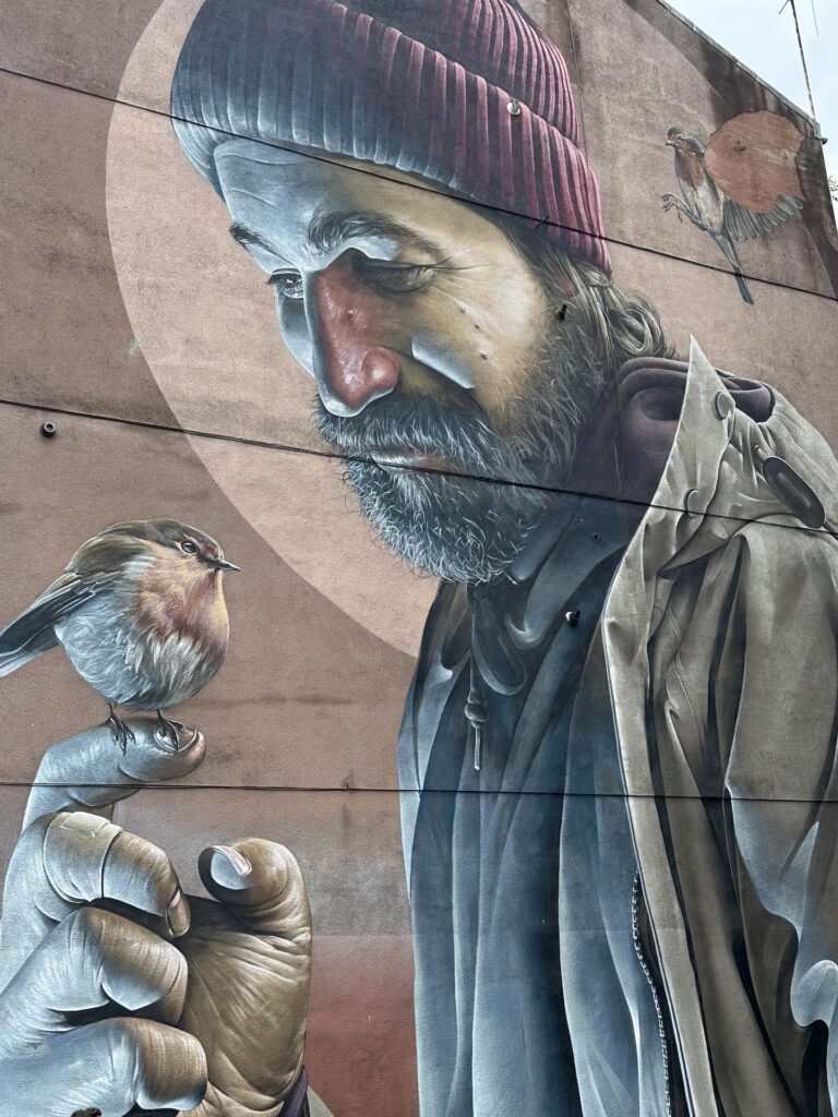 A famous street mural in Glasgow of a man with a bird resting on his finger. 