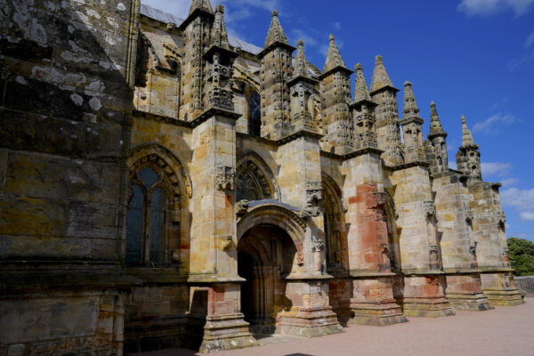 The south face of historic Roslyn Chapel features a series of square stone columns topped by intricately carved spires.