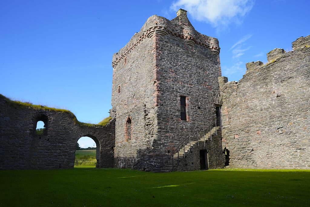 Looking across a grassy courtyard at the main keep of ruined Skipness Castle in Scotland.