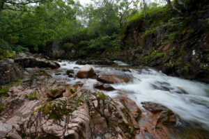 A small river cascades through a shallow rocky canyon in the West Highlands of Scotland.