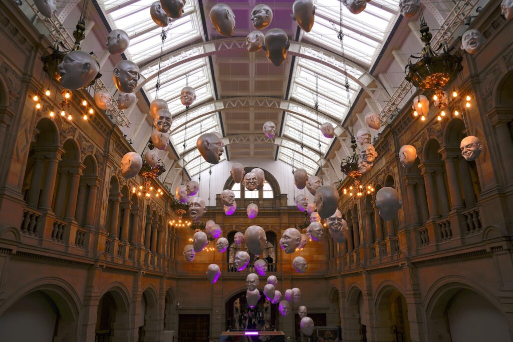 A sculptural display of heads with various facial expressions hangs from the ceiling of Glasgow's Kelvingrove Museum.