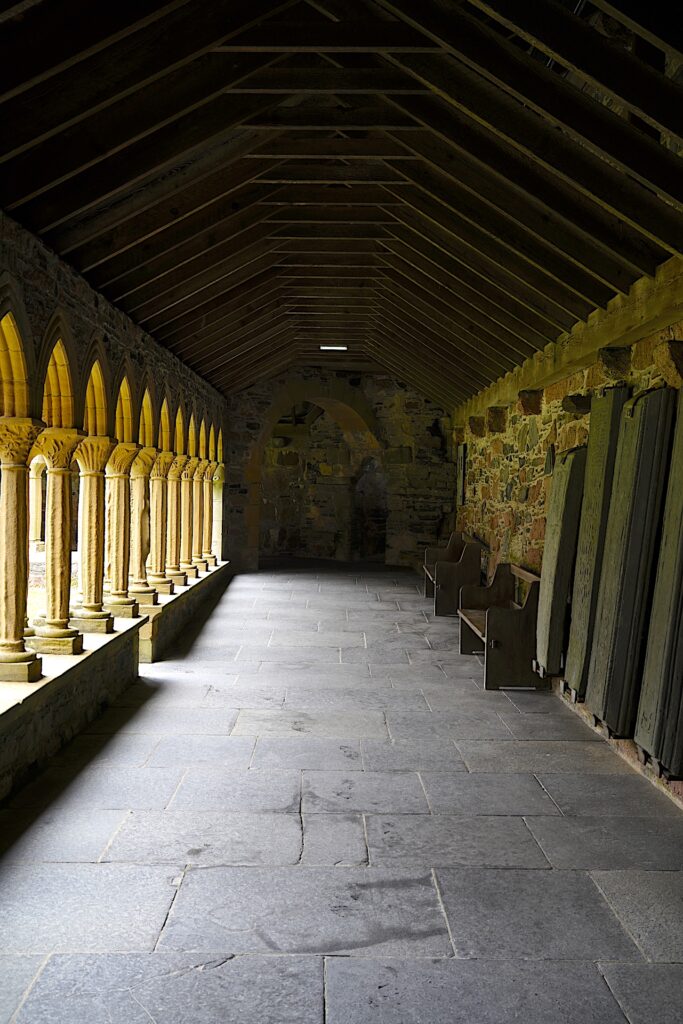 The cloister at Iona Abbey has ancient carved stone grave markers displayed against the walls.