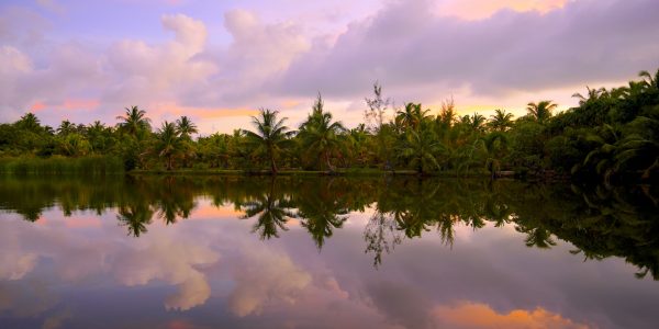 Pink and purple sunset skies are reflected in Lake Tautau, French Polynesia.